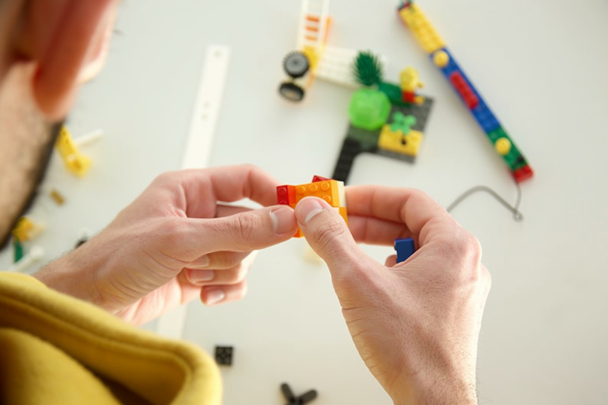 Gros plan sur deux mains qui assemblent des briques LEGOⓇ au cours d'un atelier LEGOⓇ SERIOUS PLAYⓇ pour stimuler la créativité et la collaboration à Bourges.
