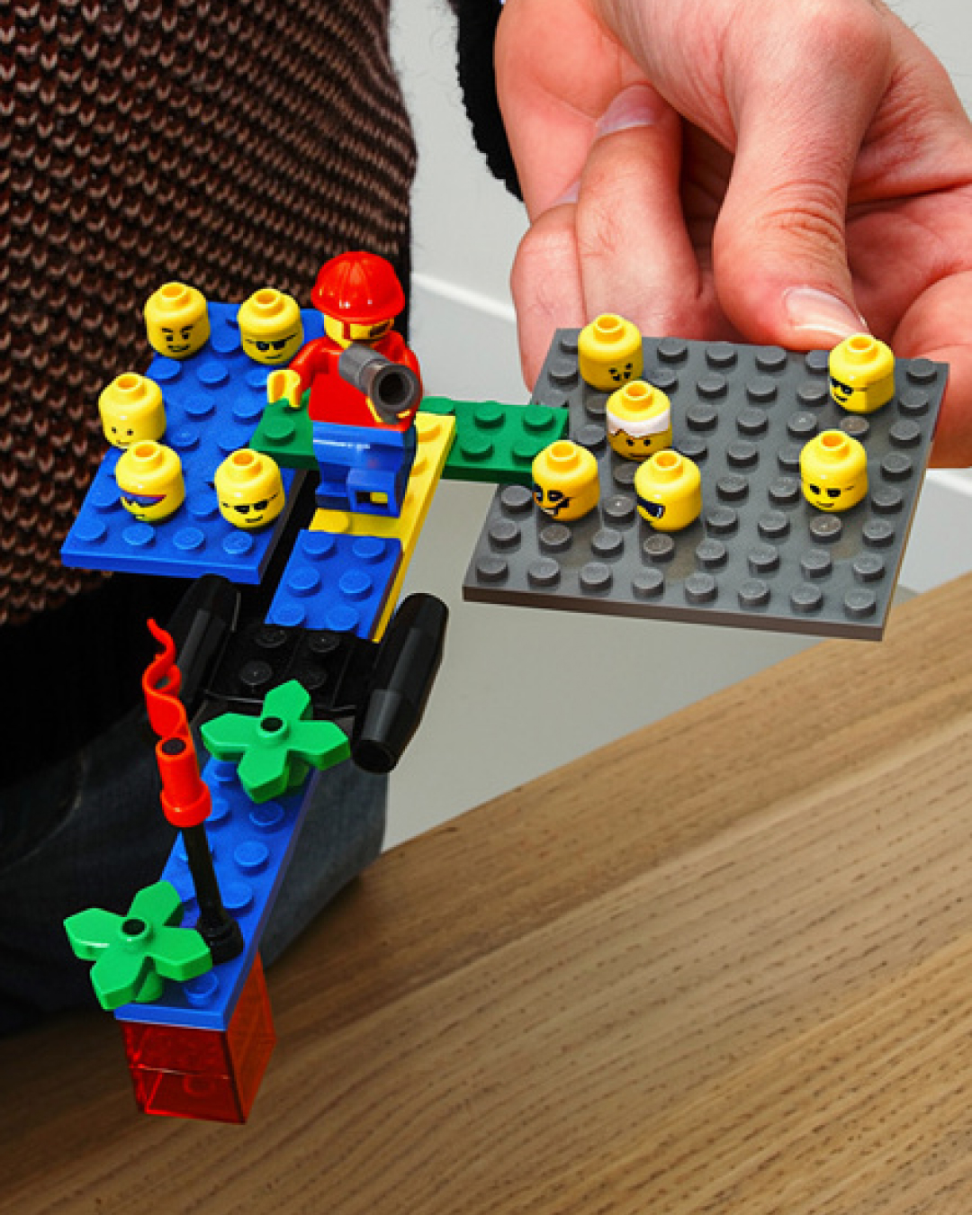 Le modèle est une construction de briques LEGOⓇ au cours d'un atelier LEGOⓇ SERIOUS PLAYⓇ à Bourges. Une main tiens le modèle qui représente deux équipes d'entreprise suite au rachat d'une entité. Un personnage mène ses équipes rassemblées vers un objectif commun.