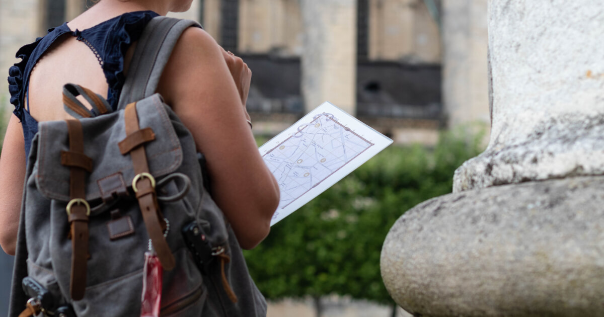 Une joueuse s’apprête à partiravec son kit de jeu, un sac à dos fermé, une carte de la zone de jeu, au départ de la place Etienne Dolet à Bourges, avec la cathédrale Saint-Etienne en arrière plan.